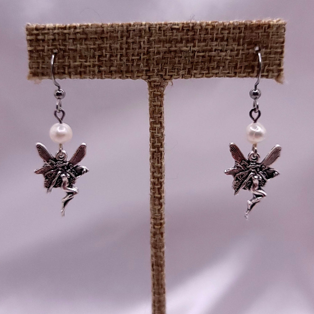 Fairy-themed dangle earrings with pearls on a brown earring stand against a neutral background