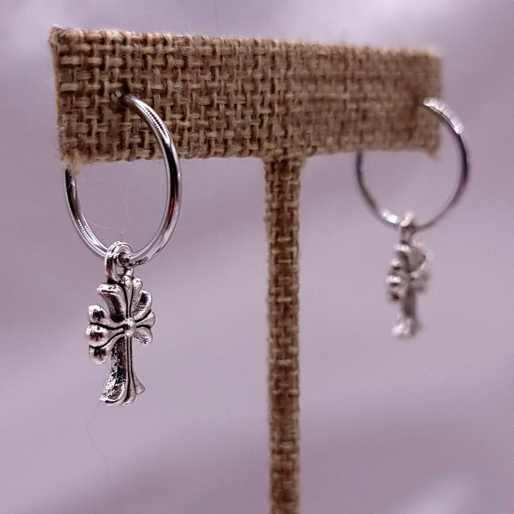 Two silver hoops earrings with cross on a white fabric background