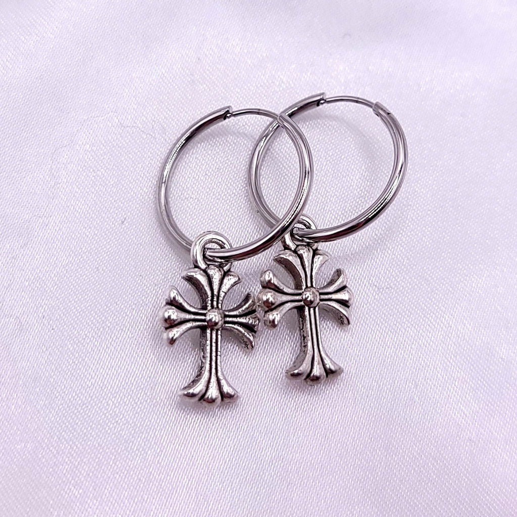 Two silver hoops earrings with cross on a white fabric background